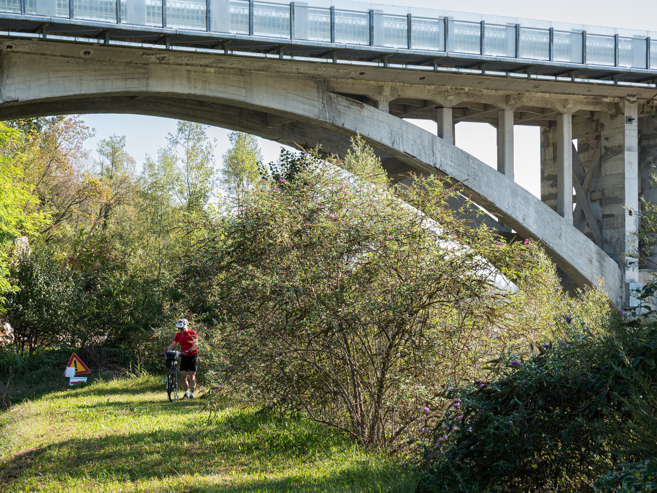 Radfahrer schiebt unter dem mächtigen Betonbogen der Brücke hindurch